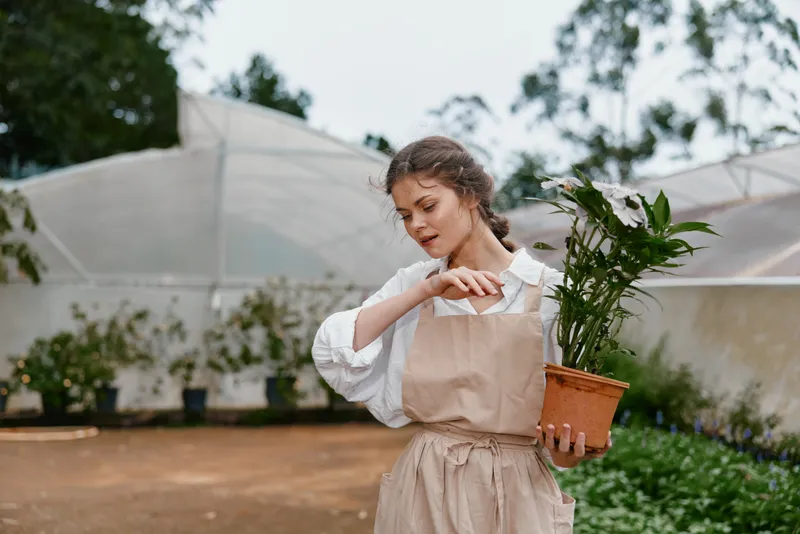 Young woman tending to plants in a greenhouse, showcasing love for gardening, nurturing nature, and sustainable living amidst greenery and natural light