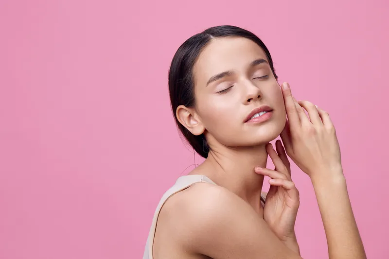 Young woman with closed eyes against a pink background, showcasing natural beauty and wellness, with soft lighting and a serene expression
