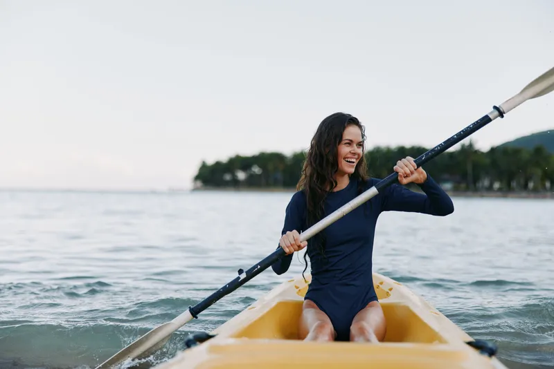 Female kayaker paddles a yellow kayak on calm water, smiling with effort as the oar slices the surface, capturing energy, focus, and outdoor adventure.