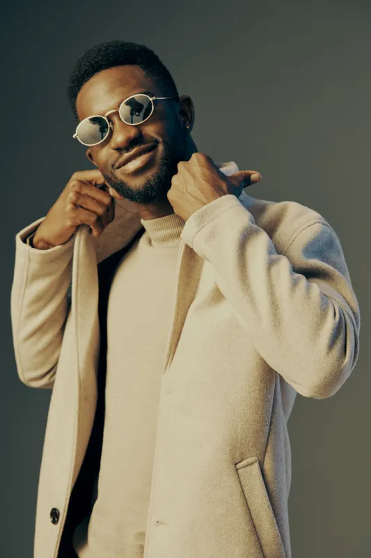 Stylish young man in a cream coat and sunglasses, exuding confidence and elegance in a soft, neutral toned background, perfect for fashion related concepts