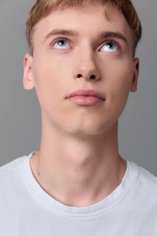 Young man gazing upward with a thoughtful expression, white tee, studio lighting, neutral backdrop, quiet moment of curiosity and reflection, modern casual mood in a controlled studio setup