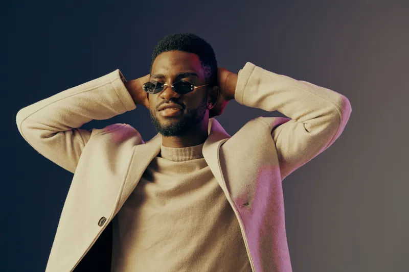 Stylish young Black man in sunglasses showcasing confidence against a gradient backdrop, exuding modern fashion and contemporary lifestyle trends