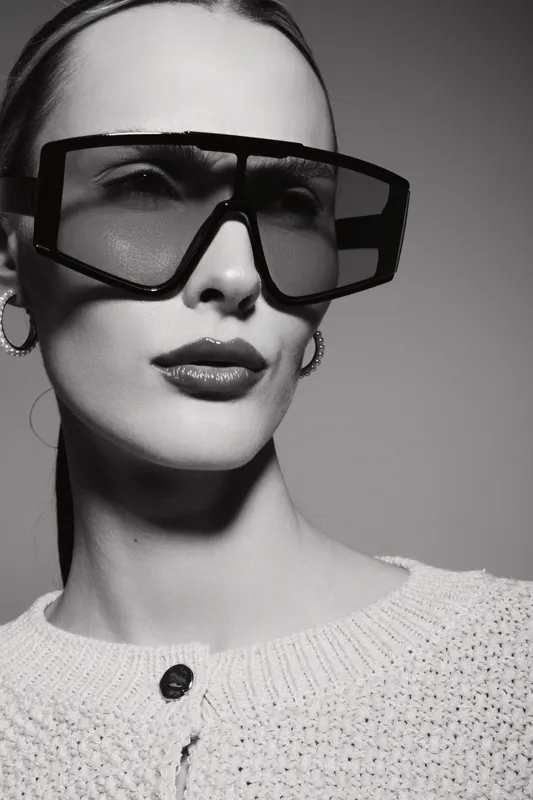 Close-up portrait of a fair-skinned Caucasian woman wearing large sunglasses and a knitted sweater in studio lighting. Fashion concept with confident expression.