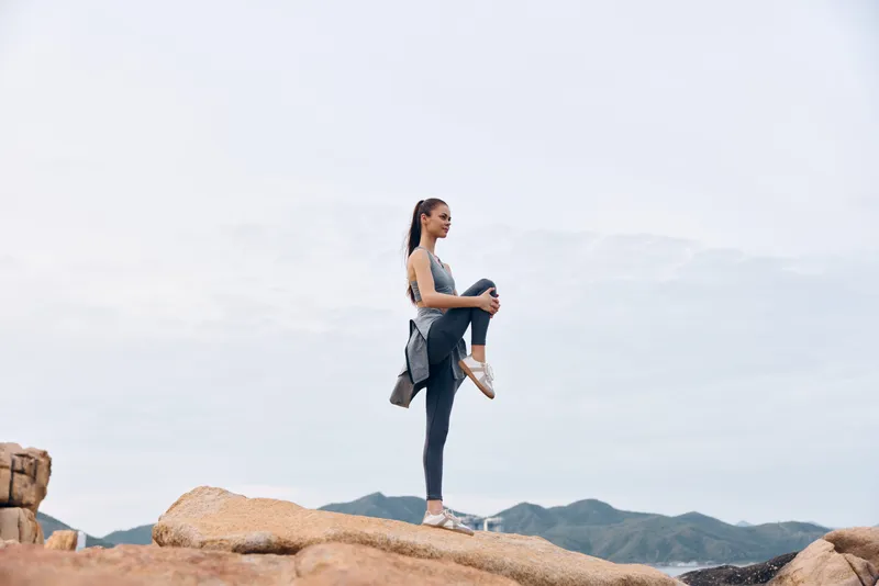 Fit young woman practicing yoga on rocky terrain in athletic wear, showcasing strength and balance against a serene natural backdrop