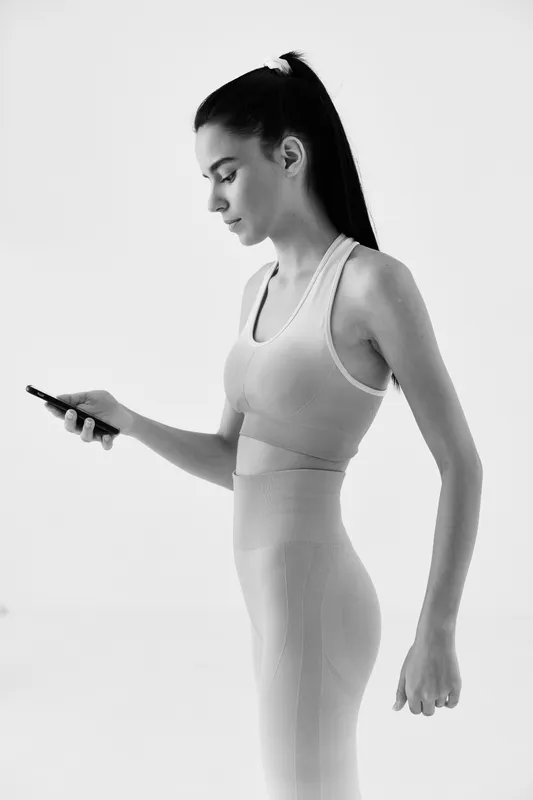 Black and white portrait of a woman sport fitness checking her smartphone, wearing seamless activewear with focused expression and long ponytail hairstyle.