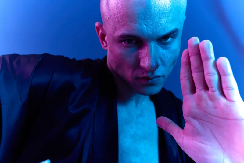 Intense man performing martial arts with a dramatic expression, showcasing his strength and focus under dynamic lighting. Captivating blue and purple tones enhance the mood.