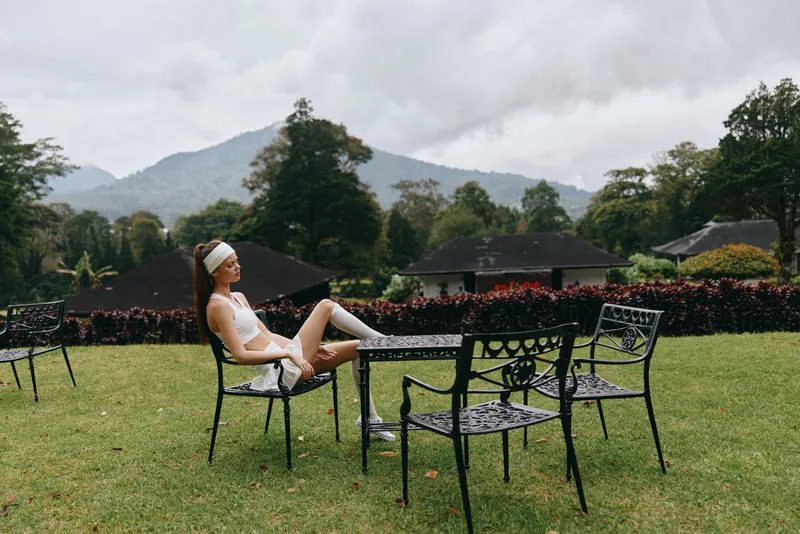 Young woman in sporty attire sitting on a chair in a serene outdoor setting, reflecting relaxation and mindfulness during a calm day