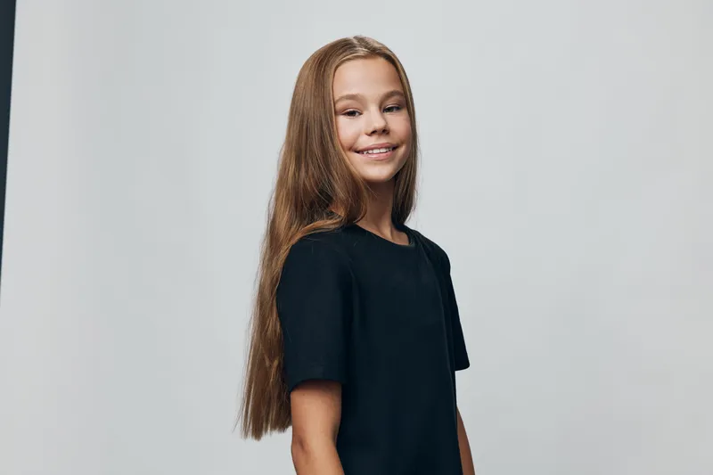 Girl with long hair smiling and standing in black t shirt against grey background for portrait and youth style in studio lighting.