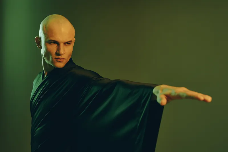 Striking man in a black robe, striking a powerful pose with a dramatic aura, emphasizing strength and focus, set against a muted backdrop.