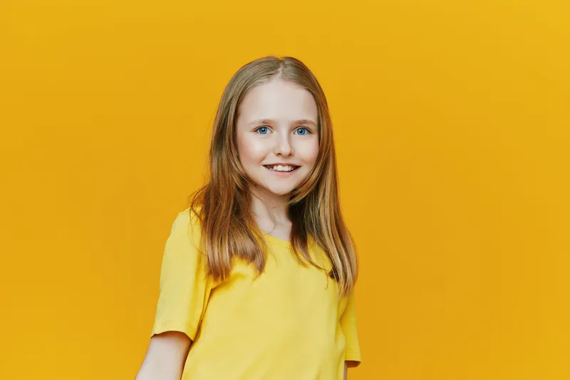 Cheerful young girl with long hair wearing a yellow t shirt, smiling against a vibrant yellow background, showcasing joy and positivity, perfect for spring themes