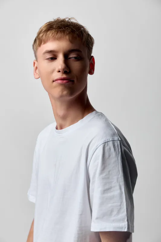 Young man in a white t shirt stands in a clean studio with a calm expression, casual fashion and minimalist backdrop, suggesting everyday style, basics, and contemporary streetwear influence