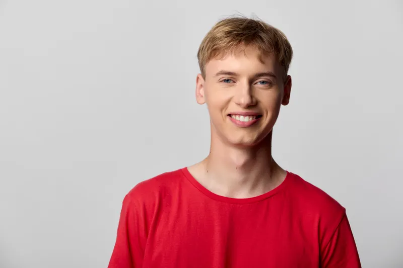 Smiling young man in a bright red shirt stands against a neutral studio backdrop, conveying casual confidence and approachable charm for lifestyle, fashion, and advertising campaigns.