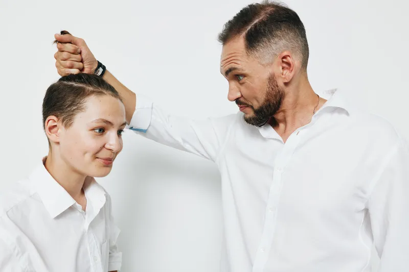 A professional man tends to a younger client in a clean studio with an isolated colored backdrop. The scene shows focus, care, and confident guidance in a business setting.