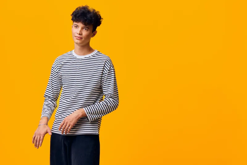 young man wearing striped shirt standing against vibrant yellow background with casual pose and thoughtful expression, modern style and bright colors