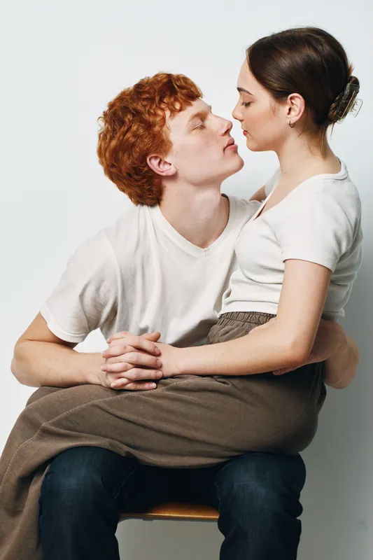 Couple sitting together and showing affection with eyes closed, intimacy and connection in casual clothes. Young man and woman in white t shirts and relaxed posture.