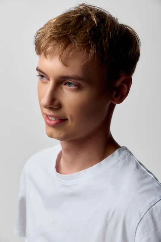 Young man in a white tshirt stands in studio lighting with a gentle smile and neutral background, clean and modern vibe, simple composition suitable for lifestyle and web use