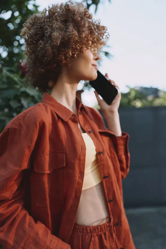 Casual woman outdoor lifestyle on phone, rust jacket, portrait style, candid moment, natural light, relaxed mood, everyday city vibe, candid urban portrait style shot