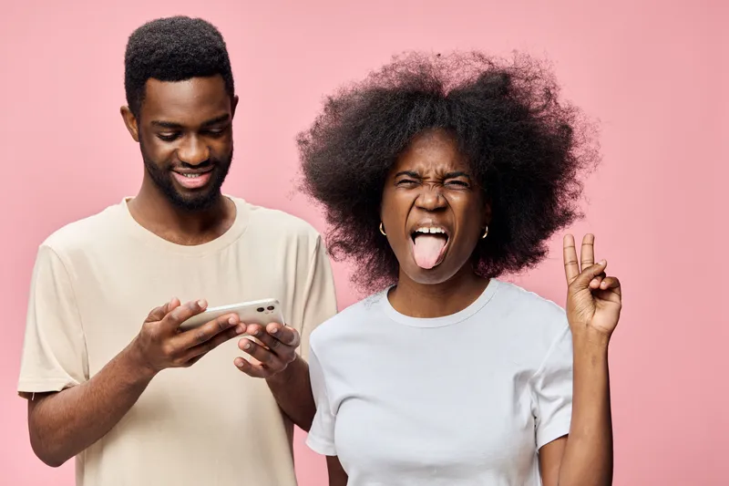 Young diverse couple with playful expressions against a pink background, showcasing joy and connection, perfect for themes of love, friendship, and modern relationships