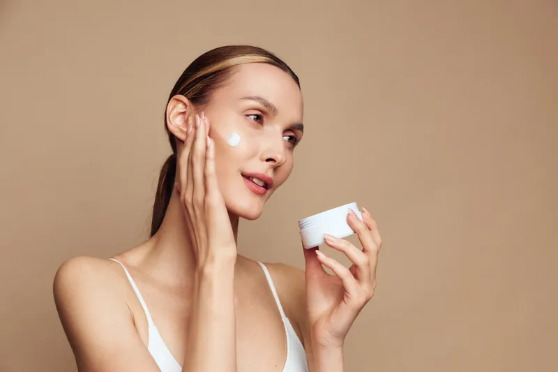 Woman applying moisturizer on clean skin, soft glow, indoor studio lighting, calm expression, skincare routine moment, natural radiance, gentle self care gesture, minimal background