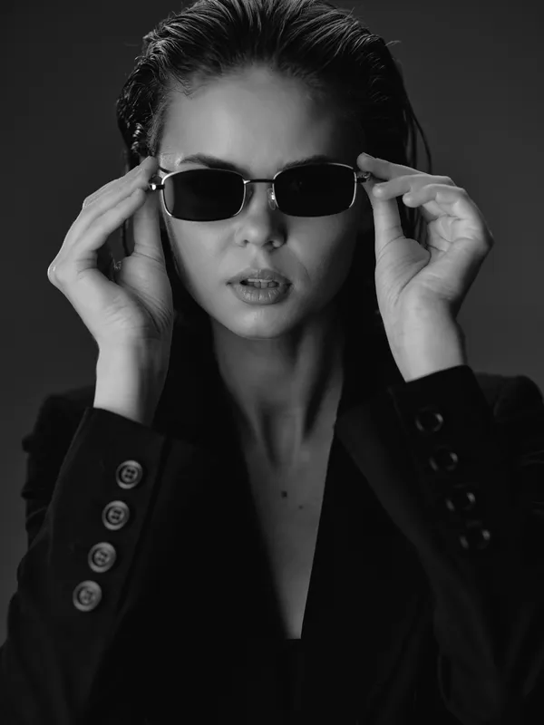 Black and white portrait of a stylish woman wearing sunglasses and a blazer with serious expression