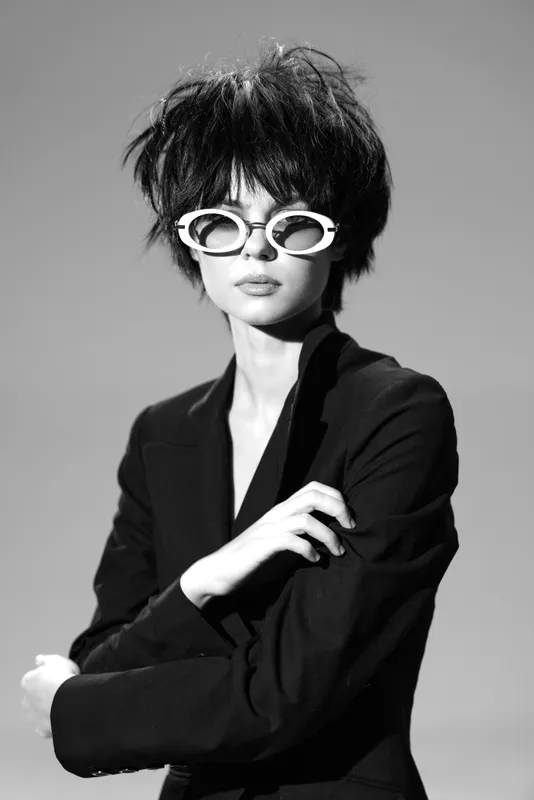 Black and white portrait of stylish woman wearing sunglasses and blazer with confident expression and vintage hairstyle