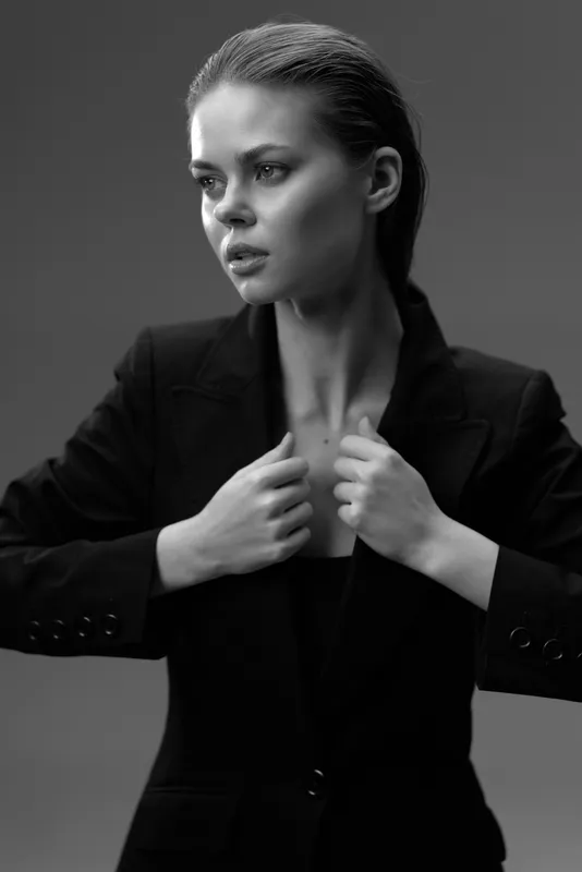 Black and white portrait of a woman in a suit jacket, looking serious and elegant, with a smooth hairstyle and minimal makeup.