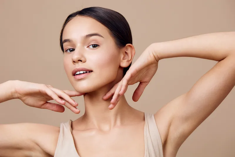 Beautiful woman with fresh skin tone posing gracefully against a soft beige background, showcasing healthy skin and natural beauty