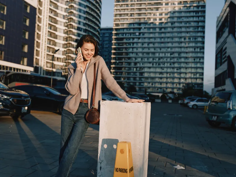 A cheerful young woman in business attire talks on her phone in a modern urban setting. She smiles warmly, exuding confidence and focus as she navigates a busy day.