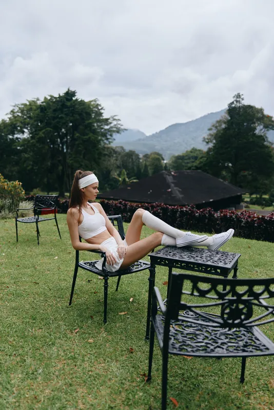 Young woman exercising outdoors in sporty outfit, sitting on a chair in a garden, showcasing healthy lifestyle and fitness concepts in a lush green environment