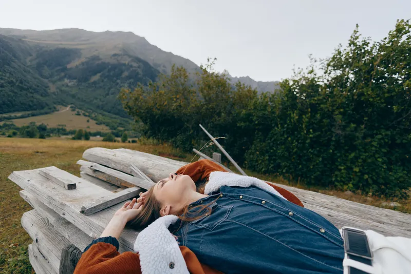 woman relax nature mountains outdoors bench travel phone, young woman lying on a wooden bench in countryside with denim jacket and mobile beside her, calm eyes closed, peaceful scenic retreat