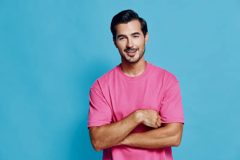 Smiling man dressed in pink t-shirt stands confidently against a vibrant blue background, showcasing a joyful expression. Lifestyle concept portrait.