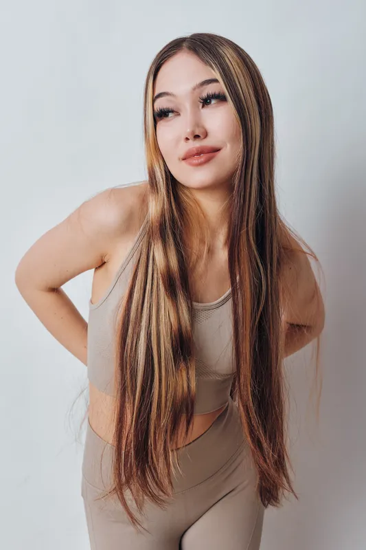 Young woman with long straight hair posing in casual sportswear against white background, looking aside with slight smile and confident posture in natural light.