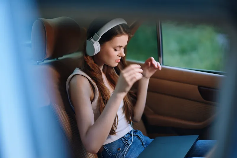 Young woman enjoying music with headphones in a car during the summer, wearing casual clothes, lost in thought, relaxed and content.