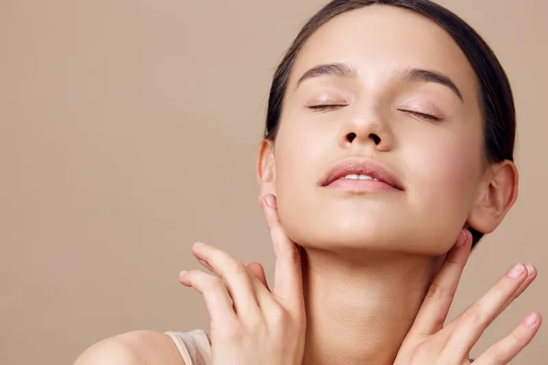 Young model with smooth skin and closed eyes, conveying relaxation and beauty, set against a soft beige background highlighting natural skincare and self care