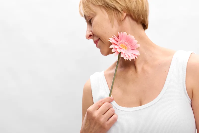 Woman in profile holds a pink flower, smiling softly, closeup on gentle tenderness, spring mood, natural beauty, minimal plain background, daylight