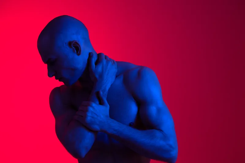A striking blue-toned image of a man, showcasing strong muscles against a vibrant red backdrop. The composition emphasizes emotion and body language beautifully.