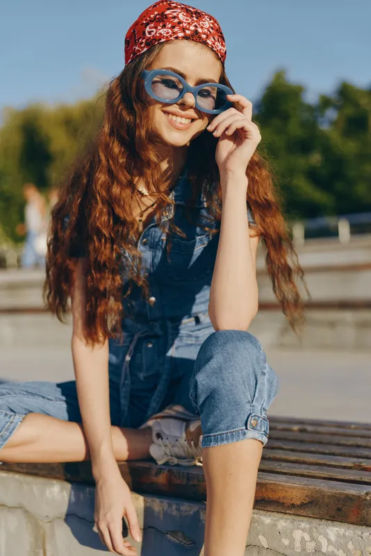 lifestyle woman wearing modern boho-western denim street style outfit with blue sunglasses and red bandana in warm sunny outdoor urban setting, film color effect
