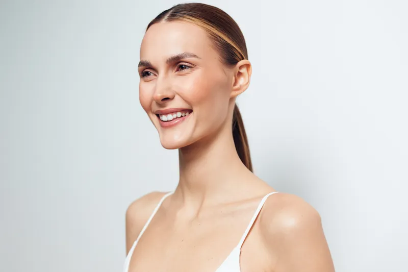 Young woman smiling in studio portrait with natural light soft skin care glow beauty wellness mood minimal background close up head and shoulders calm confident expression female