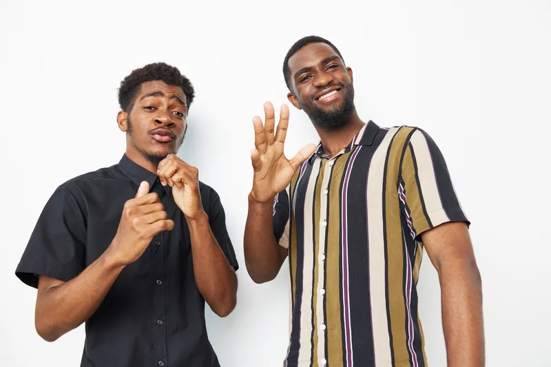Two black men smiling and posing cheerfully against a light background, showcasing joy and camaraderie. A vibrant, energetic moment captured beautifully.