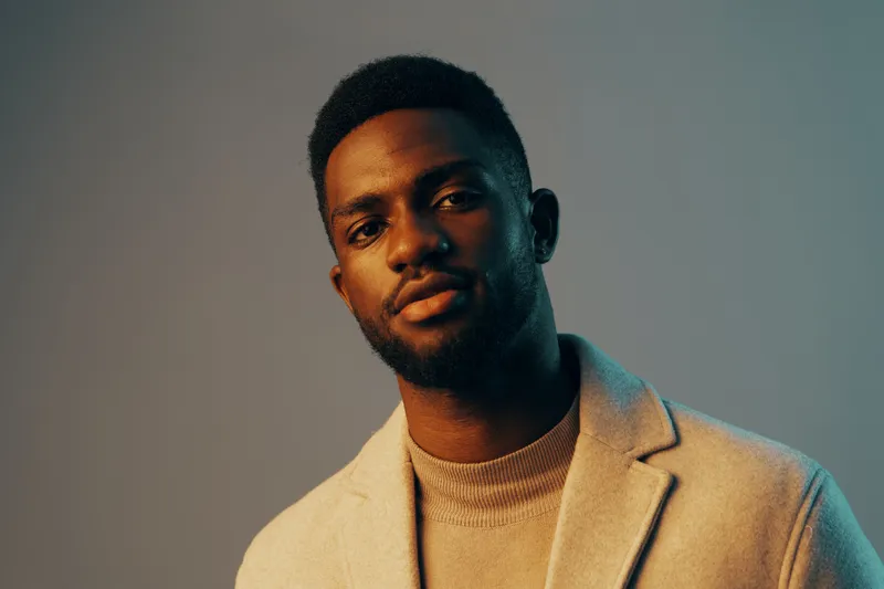 Confident young Black man in stylish winter attire against a soft gradient backdrop, showcasing warmth and modern elegance, ideal for fashion and lifestyle themes