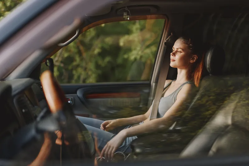 Relaxed woman sitting in a car, enjoying a moment of peace in nature, wearing a casual outfit with soft lighting, reflecting tranquility and serenity