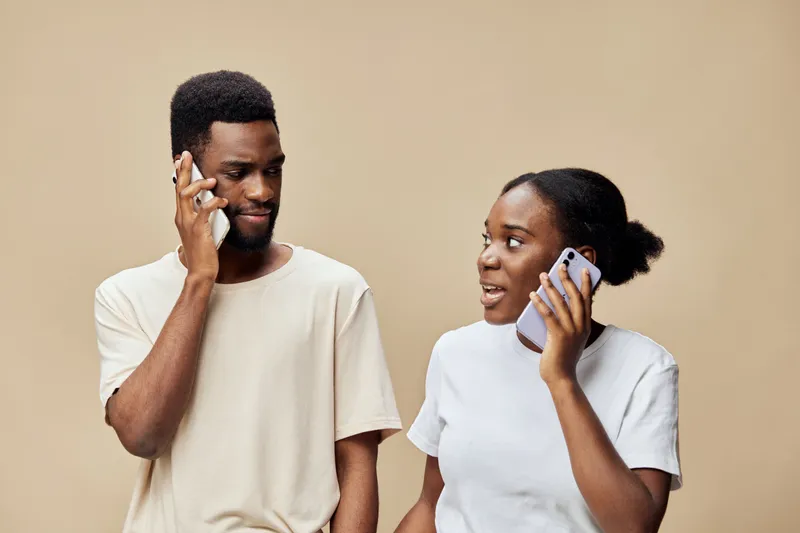 Young African American couple talking on the phone, dressed in casual clothing against a neutral brown background, showcasing connection and communication