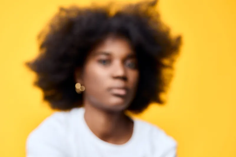 Young Black woman with curly hair against a vibrant yellow background, expressing confidence and self assurance while wearing a casual white shirt