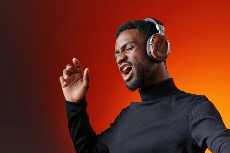 A joyful Black man enjoying music with headphones against an orange gradient background, exuding passion and energy while singing with enthusiasm