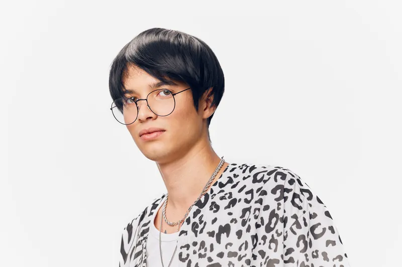young man wearing glasses in leopard print shirt with silver chains on white background, stylish and modern portrait