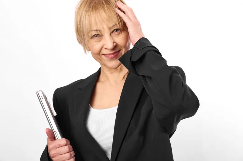 An elderly woman looking stressed, hand on forehead, holding a smartphone, shows worry and headache, exhausted portrait, concept of stress and mental fatigue, aging, communication
