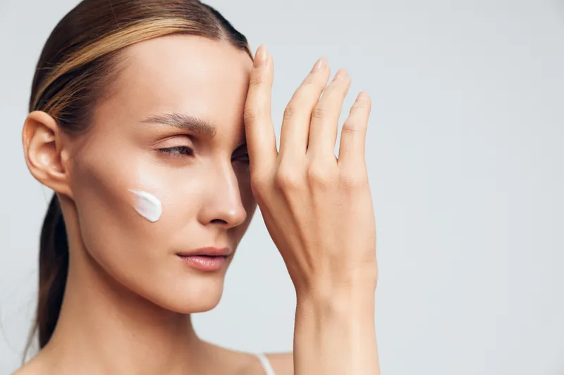 A calm woman applies moisturizer on her cheek, emphasizing a gentle skincare routine and self care. Close-up portrait showcasing healthy skin and daily beauty ritual.