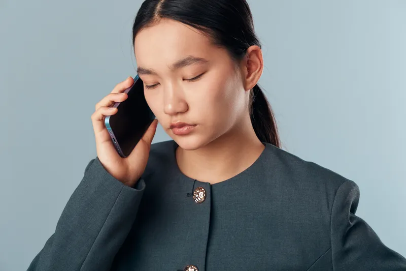 Woman in gray jacket with eyes closed talking on smartphone, communication, connection and technology concept. Portrait of concentrated young female in studio with mobile device for conversation.