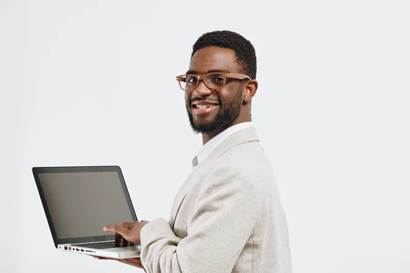 Smiling man with glasses holding open laptop isolated on plain white background. Studio portrait of professional young African American male in business casual attire, technology, communication, work,