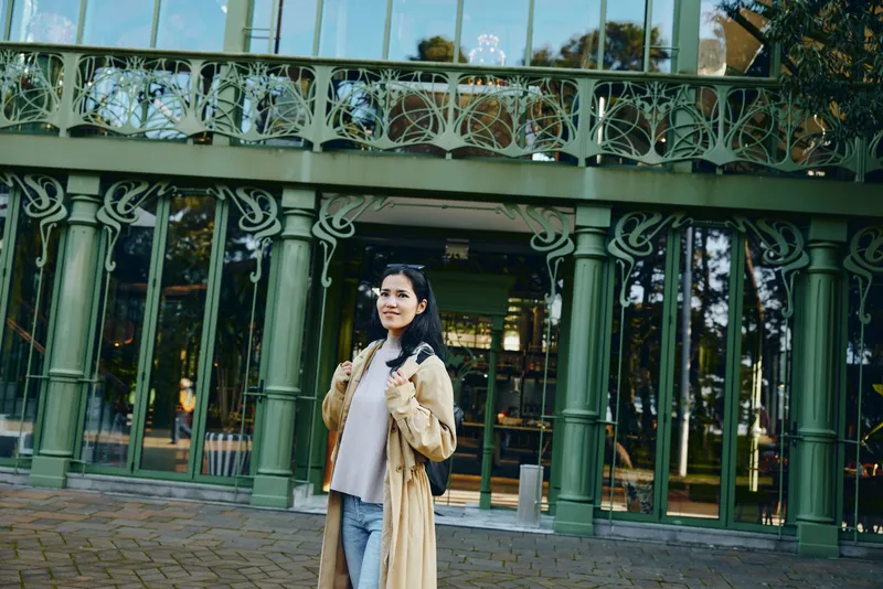 Woman in fur coat posing outside a green glass storefront, ornate architecture and urban street scene, chic style under daylight glow, confident expression, fashion moment captured in street